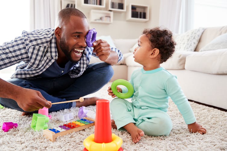 Man and toddler sat on floor playing with toys.