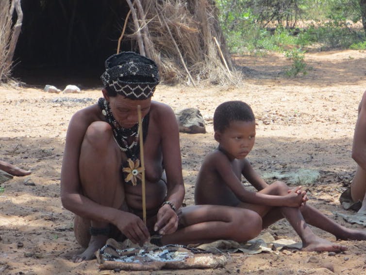 ǃKung woman making jewellery next to a child.