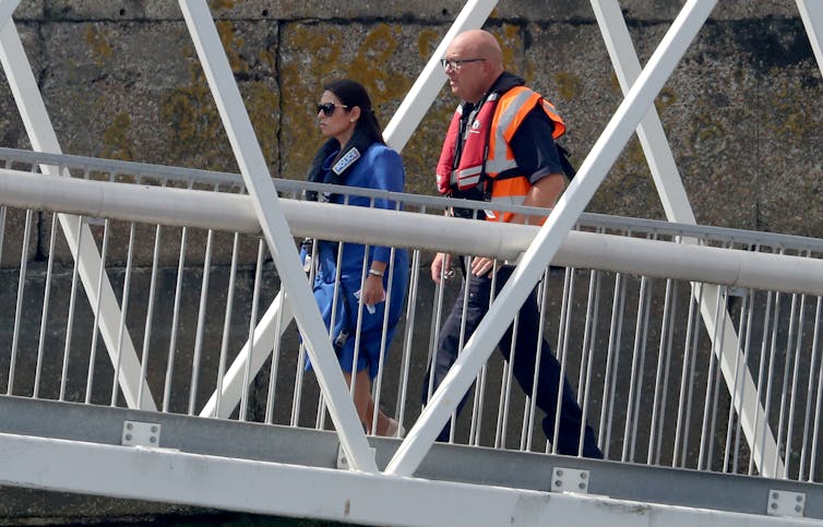 Priti Patel walks with a man in a life jacket.