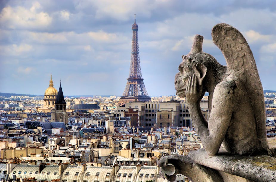 Stone gargoyle looking out over Paris and the Eiffel Tower.