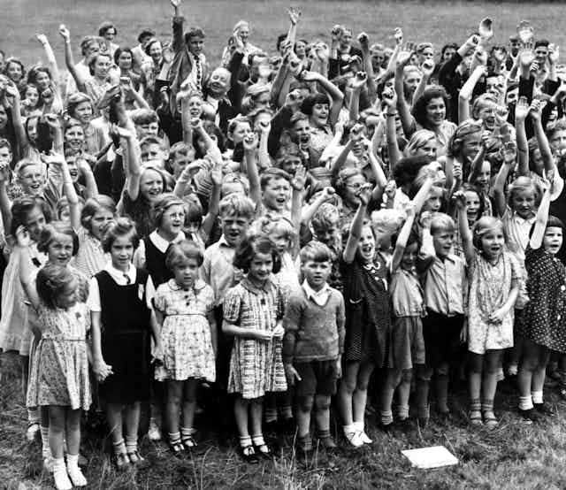 Group of young boys and girls in a field with arms raised