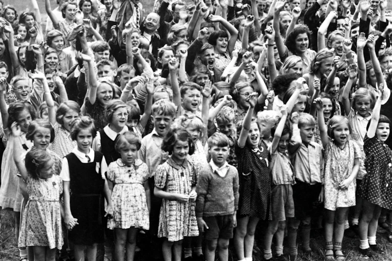 Group of young boys and girls in a field with arms raised