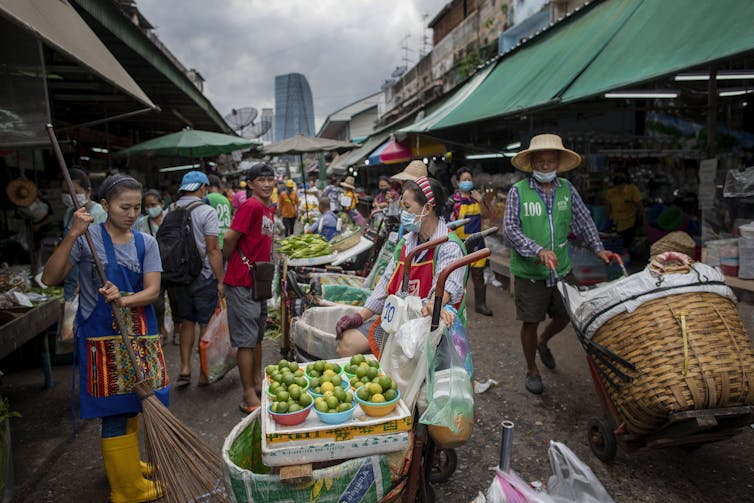 Shoppers and vendors in an open-air market, with fruits and vegetables nearby