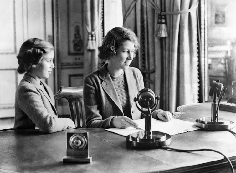 Princess Elizabeth and Princess Margaret at a desk in Windsor Castle with a radio microphone.