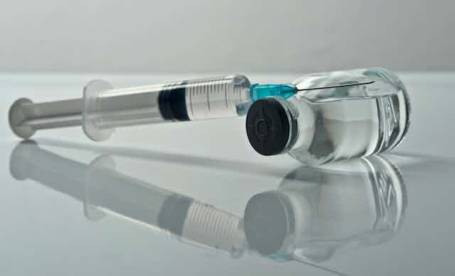 A syringe leaning on a vial against a gray background.