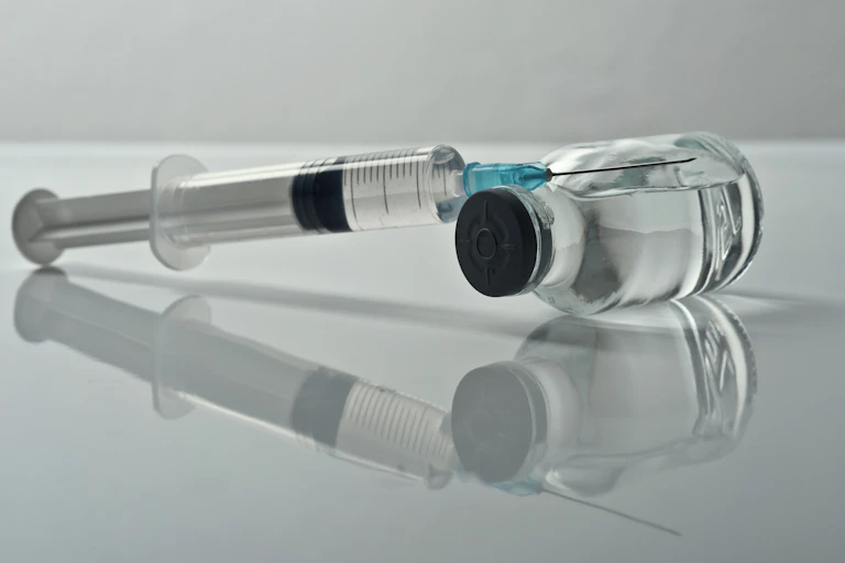 A syringe leaning on a vial against a gray background.