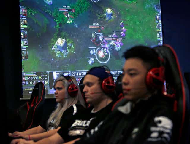 College videogame team members, one female and two male, sit in a row wearing headsets