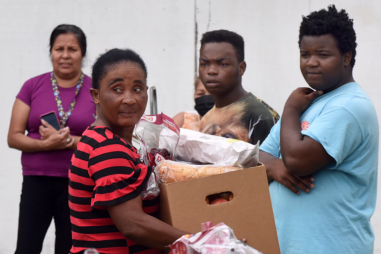 Four people at a food bank, one of whom holds a box of food.