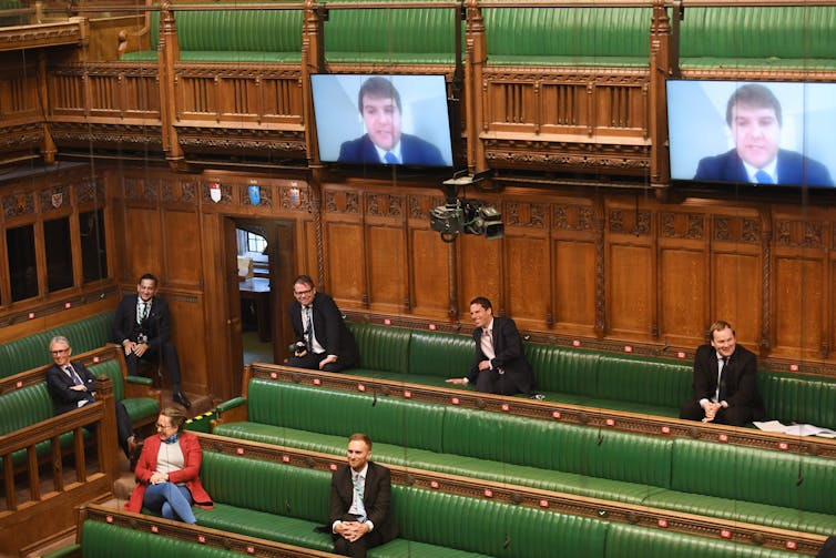 House of Commons chamber with MPs spaced out on benches and appearing on video screens.