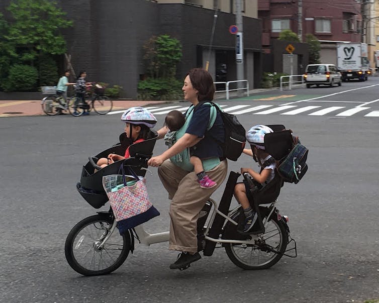 A young woman riding a bike that also holds three young children.