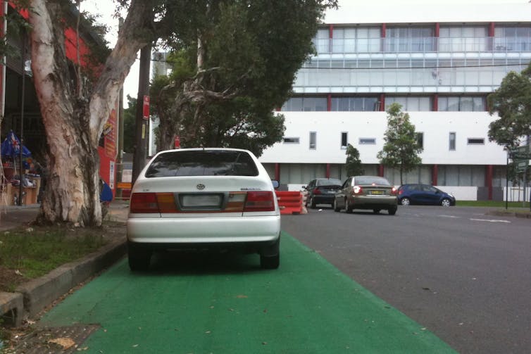 A white car parked in a bike lane.