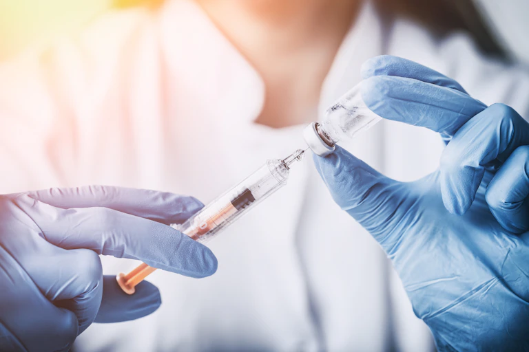 Gloved hands holding vaccine and needle.
