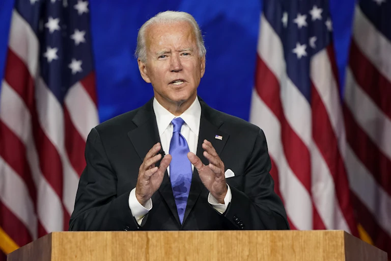 Biden stands at a podium flanked by American flags.