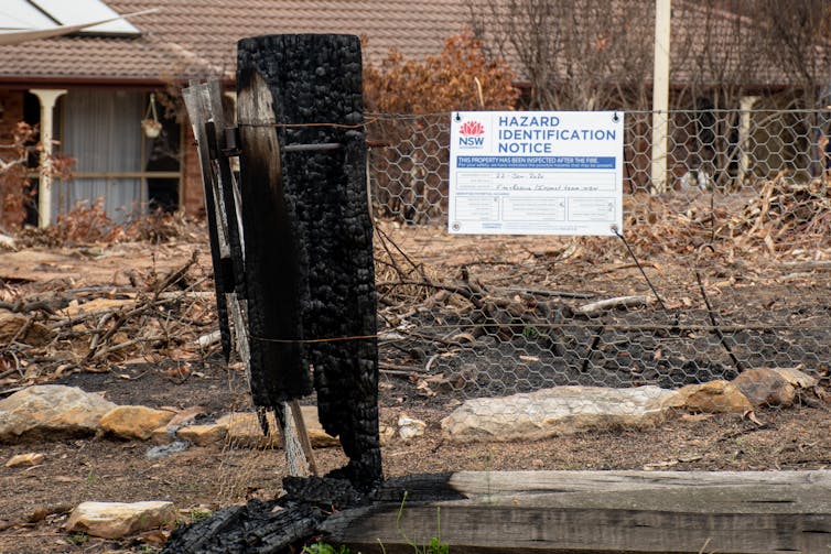 Bushfire debris outside a house, wiht a hazard warning sign in front.