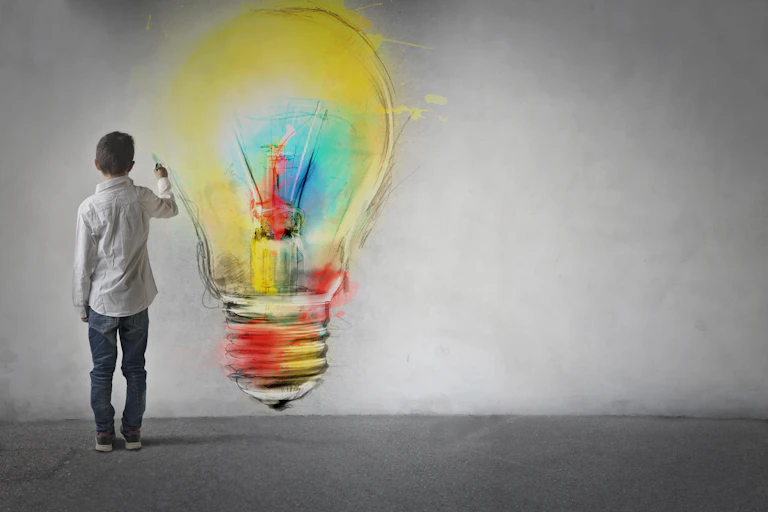 The back of a young boy drawing a light bulb on the wall.