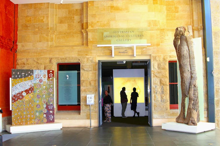 People stand in a gallery among artworks. A sign reads 'Aboriginal Culture Art Gallery'