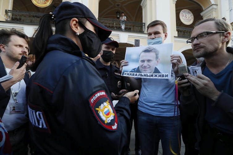 Man surrounded by police and journalists holding photo of Alexei Navalny