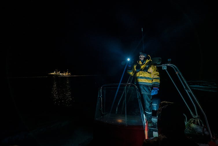 A man on a boat stands with a torch, looking into the polar night.