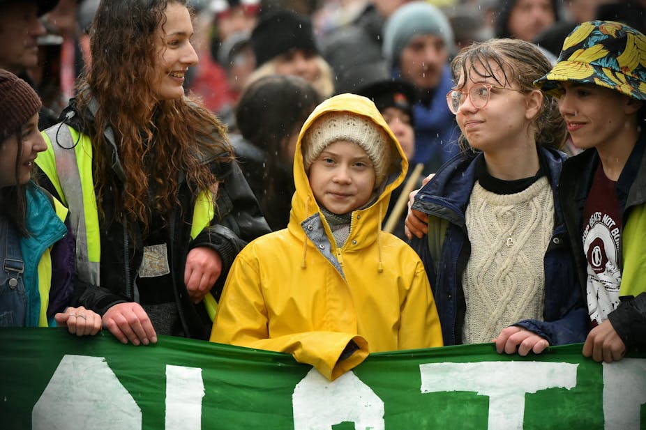 Greta Thunberg stands behind a green banner surrounded by other young activists.