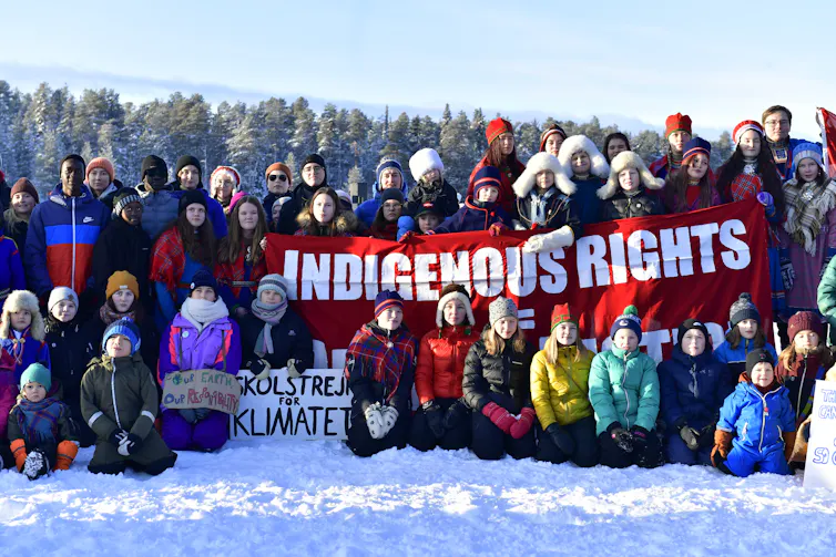 Young Sami people surround a banner reading 'indigenous rights'.