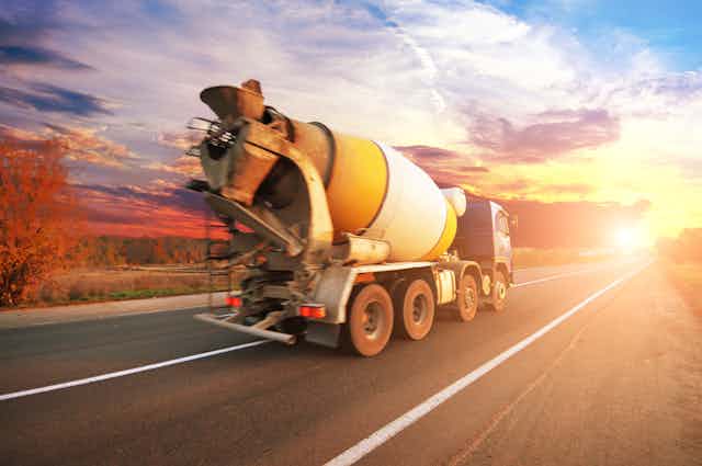 Cement mixer truck drives on road towards sunset