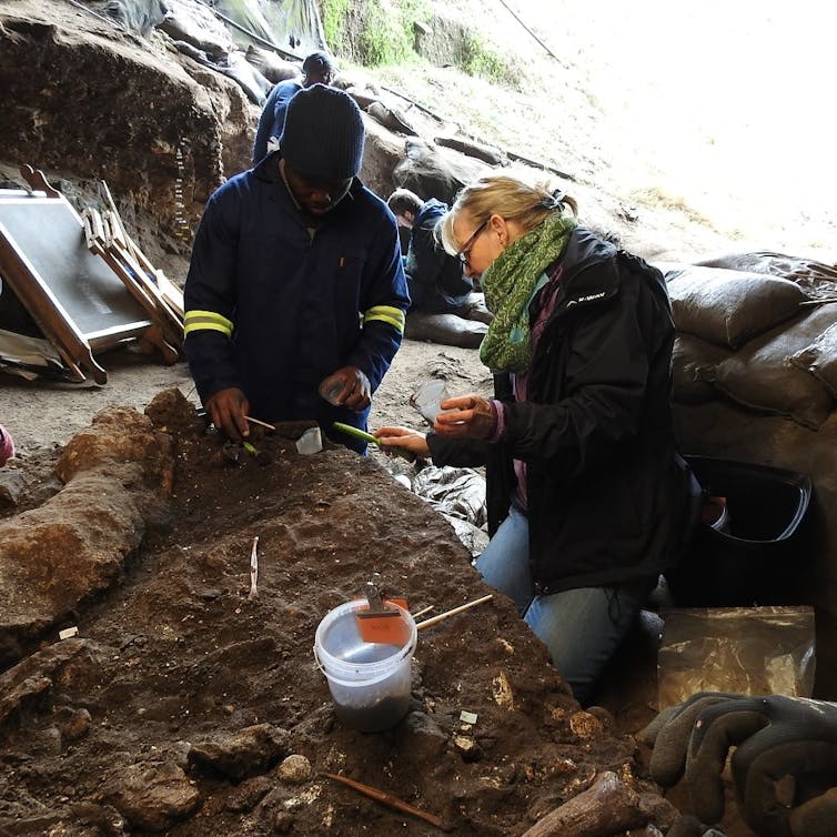 A man and a woman warmly dressed sorting through dug up objects in a cave.