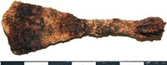 A small, brown, rusty metal object in the shape of an oar.