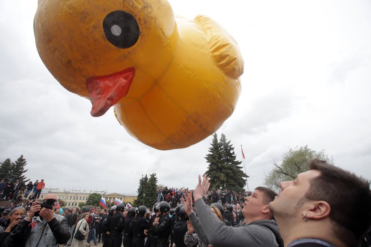 A large rubber duck floating above a political opposition rally.