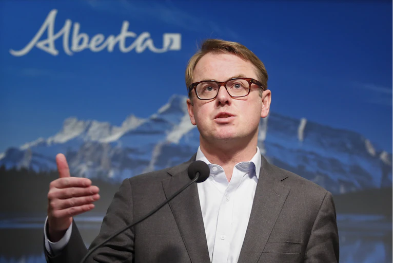 Alberta Minister of Health Tyler Shandro standing at a podium in front of a backdrop of mountains and the word 'Alberta'