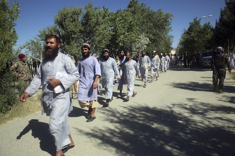 Bearded Taliban detainees walk in a single-file line after being released from prison.