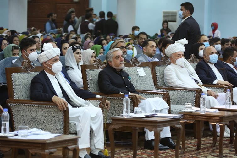 The Afghan president, several other government officials and the Afghan public sit listening in a large assembly, wearing masks
