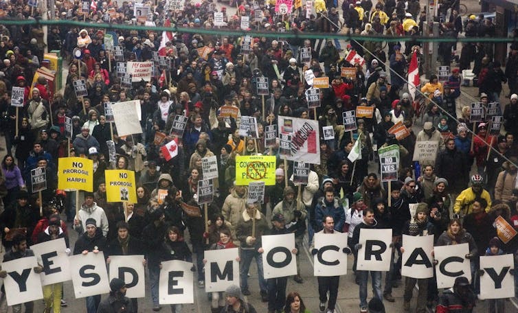 Large crowd of people marching down a street carrying signs that say, 'Yes Democracy'