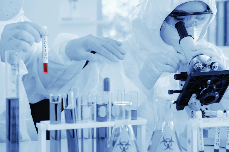 scientist in biohazard protection clothing analyzing covid 19 blood sample with microscope