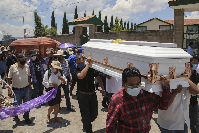 Men in face masks carry two coffins, one white and one mahogany