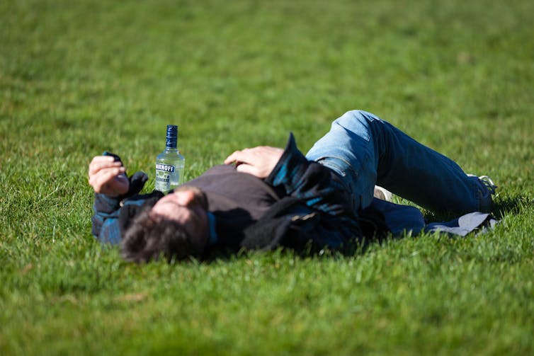 A man lies on the grass with a bottle of vodka next to him.