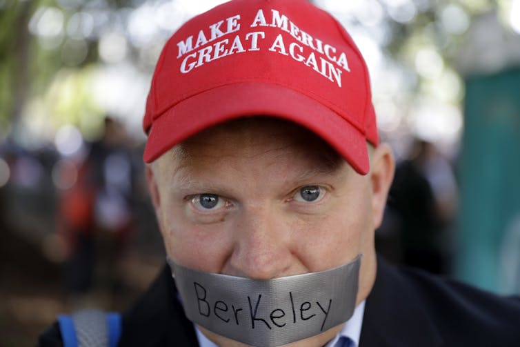 Man wearing 'Make America Great Again' with tape over his mouth with the word 'Berkeley' on it.