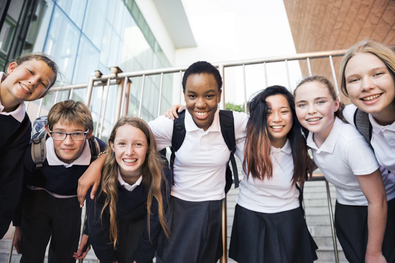 A group of school students with their arms around each other, bending down and smiling at the camera.