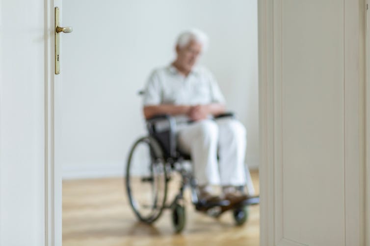 Blurred view of a man sitting in wheelchair through a doorway.