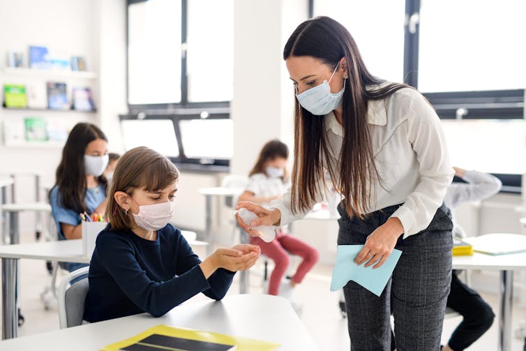 A teacher and student in a classroom wearing face masks.