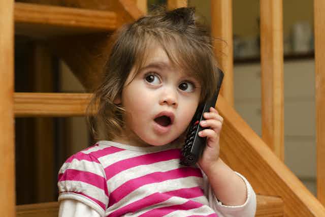 A toddler talks on a phone.