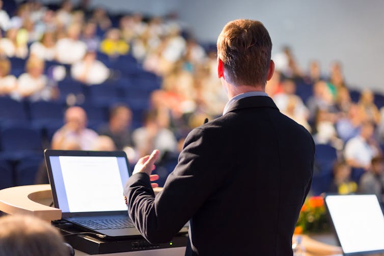 A man speaking before a crowded lecture theatre.