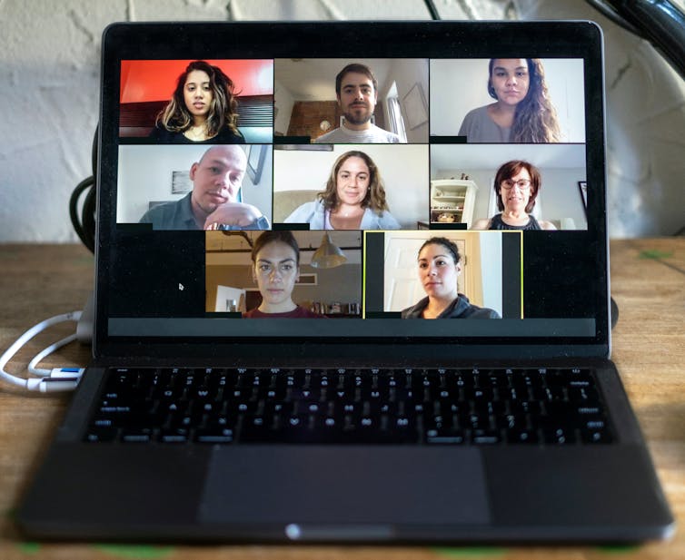 A laptop computer on a desk showing several people connecting separately from home.