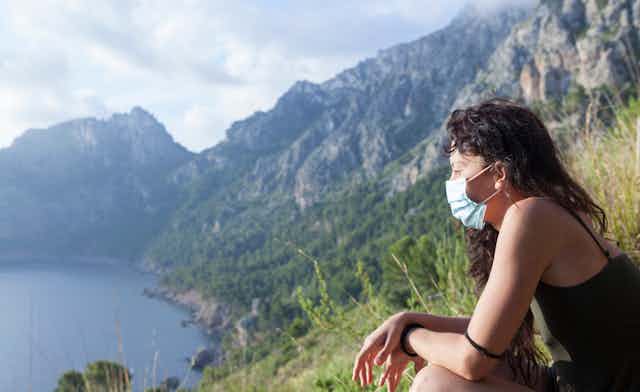 Mujer con mascarilla contemplando un paisaje de montañas y mar.