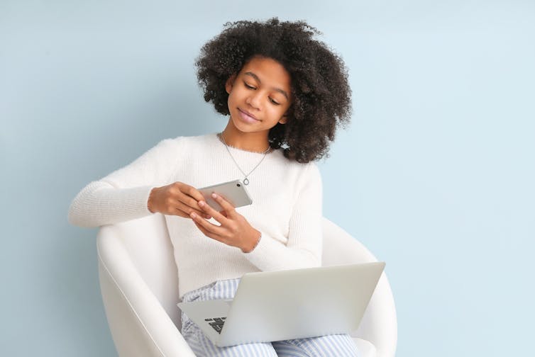 Teenager with phone and laptop on lap