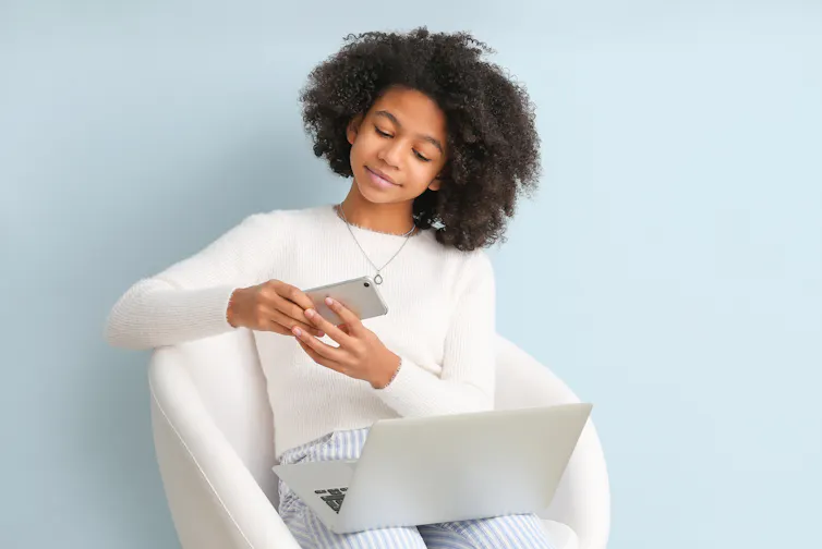 Teenager with phone and laptop on lap