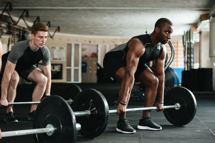 Two men lifting barbell with weights.