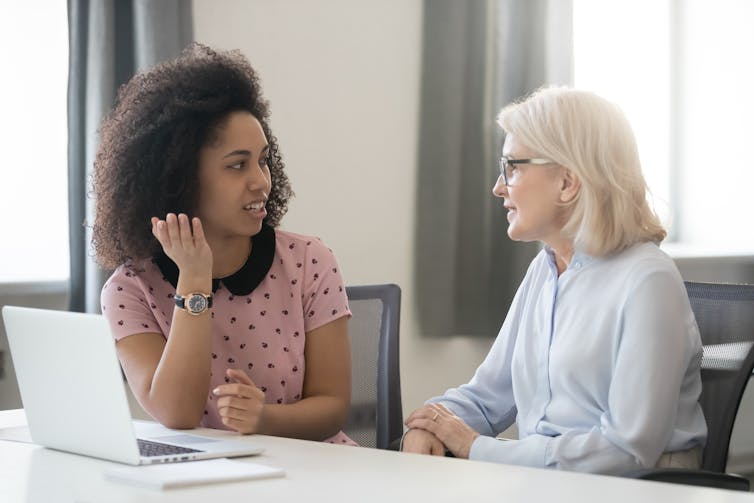 A younger woman and an older woman sitting and talking at work