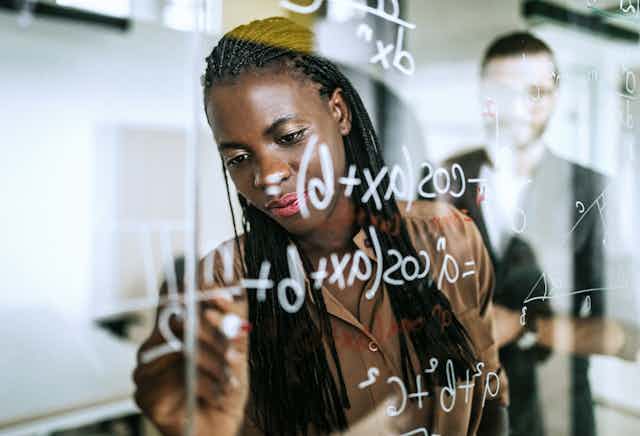 A woman writes a math problem on a glassboard.