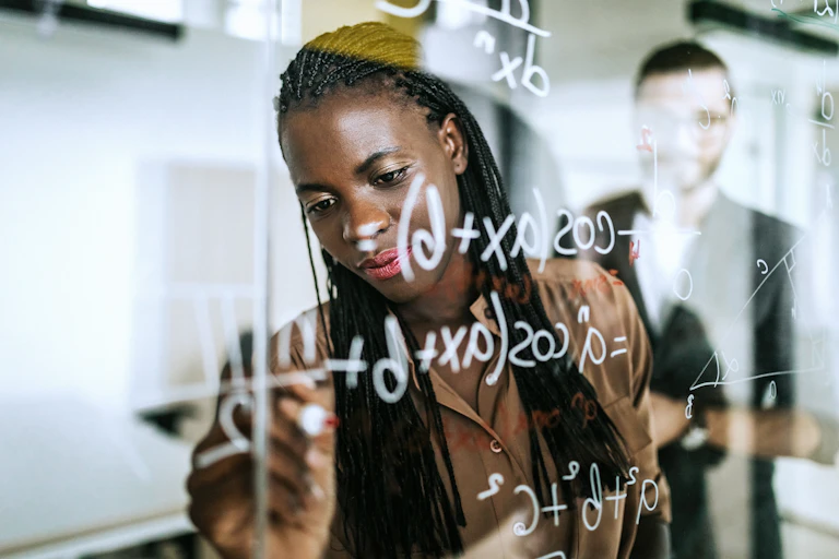 A woman writes a math problem on a glassboard.