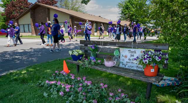Nurses dressed in purple and carrying purple balloons march in front of a long-term care home.